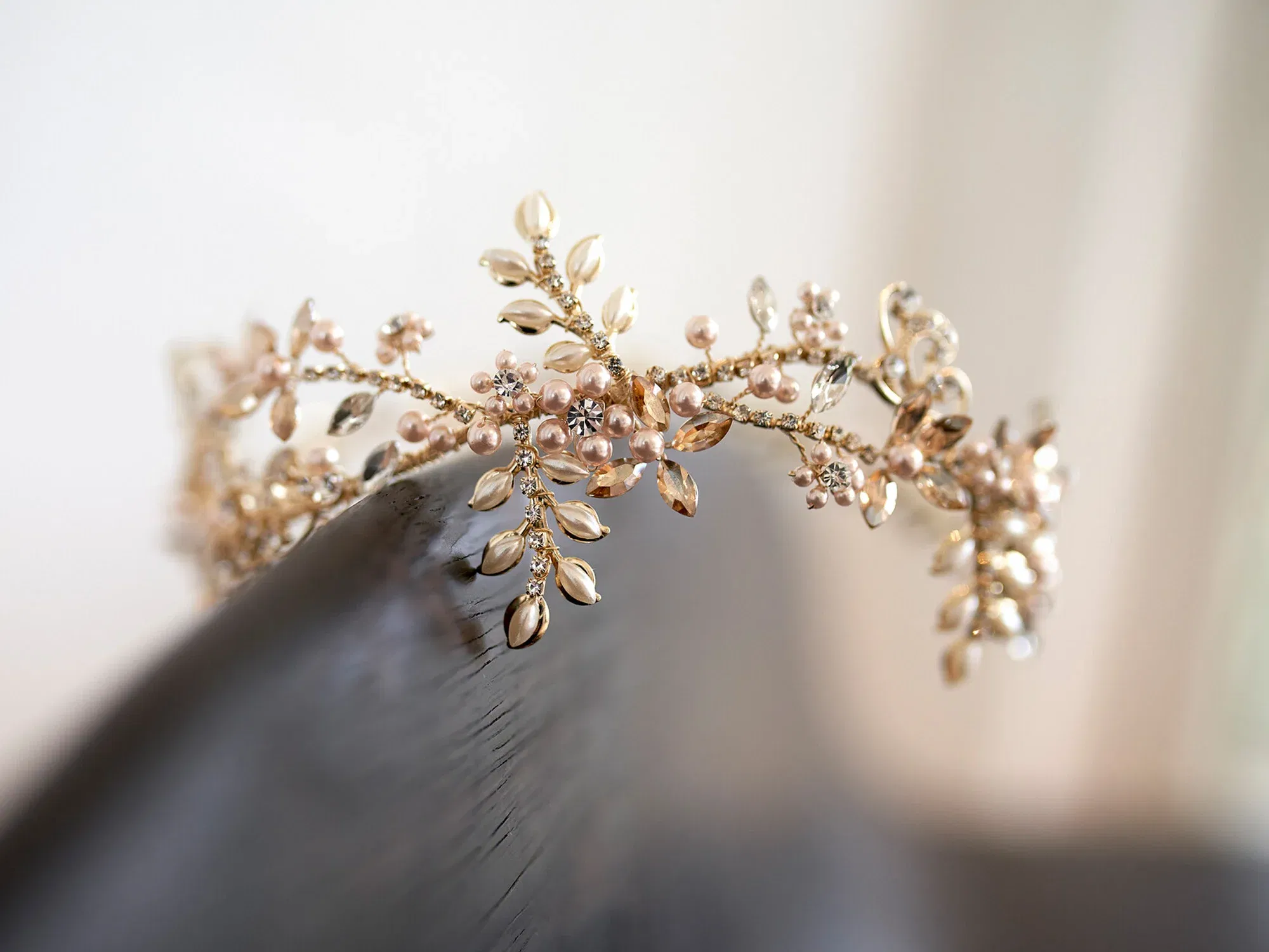 Elegante goldene Tiara mit filigranen Perlen und Kristallen im Blütenmotiv, die auf einem Holzuntergrund arrangiert ist. Ein zauberhaftes Accessoire für Bräute.