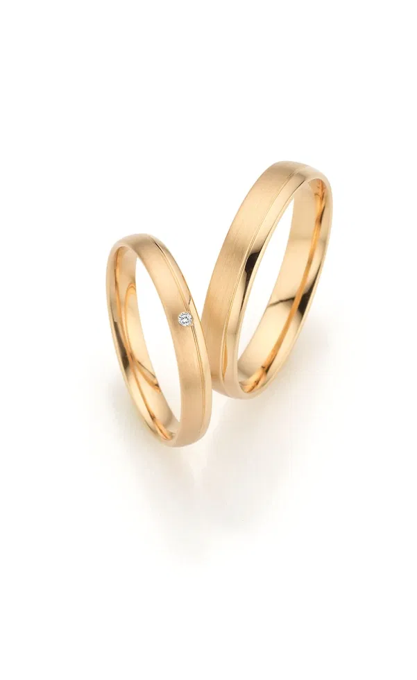 Zwei klassische Eheringe aus Gelbgold mit matter Oberfläche, einer davon mit dezentem Diamanten, vor hellem Hintergrund fotografiert.