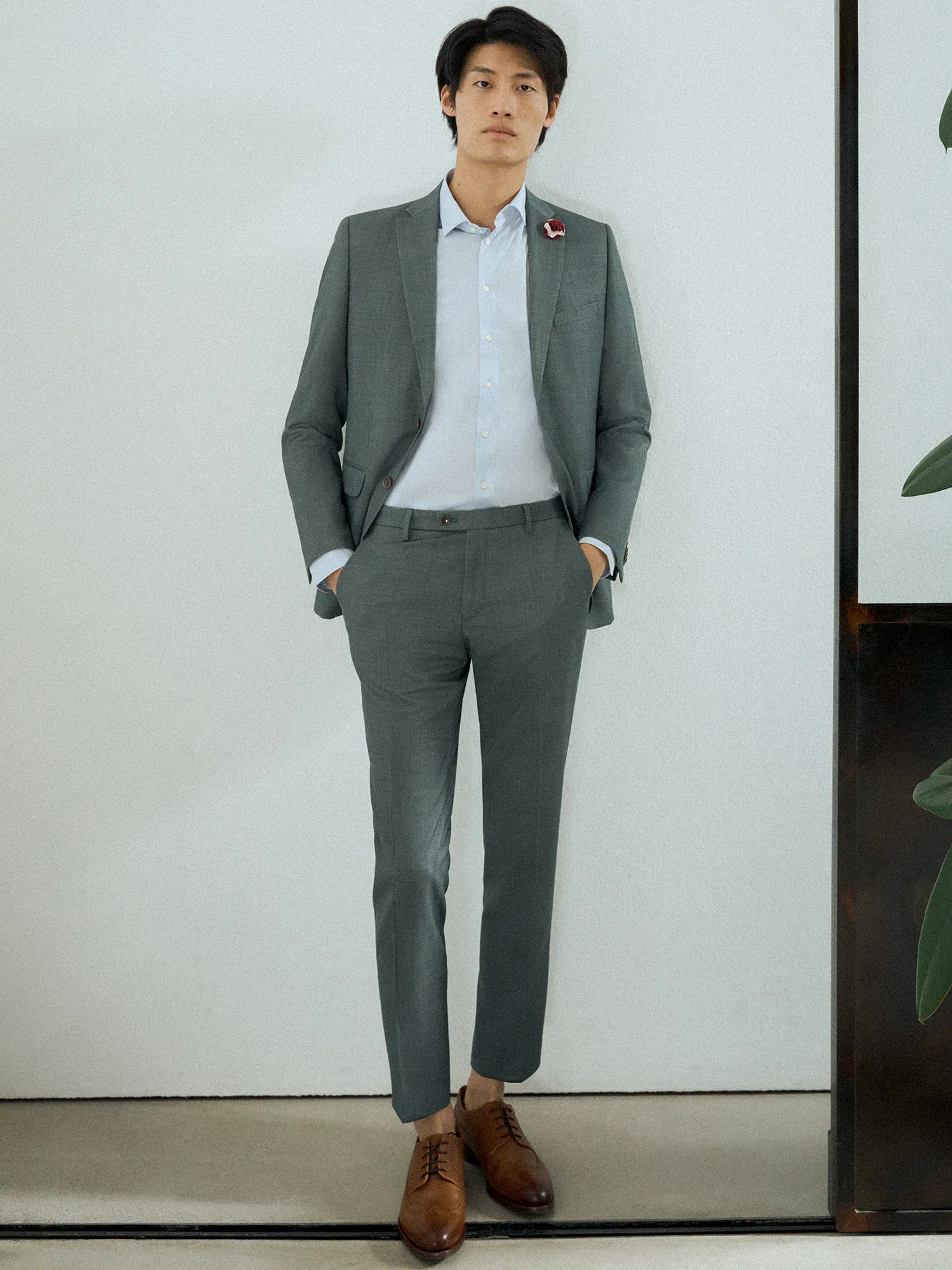 Eleganter junger Mann in einem grauen Business-Anzug, der sich lässig gegen eine Wand lehnt, mit braunen Schnürschuhen kombiniert.