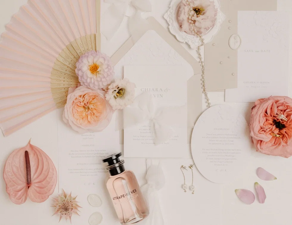 Stilvolle Flatlay-Komposition aus Hochzeits-Papeterie mit Einladungskarten, Save-the-Date, Blüten, Parfum und Schmuck in sanften Pastelltönen.