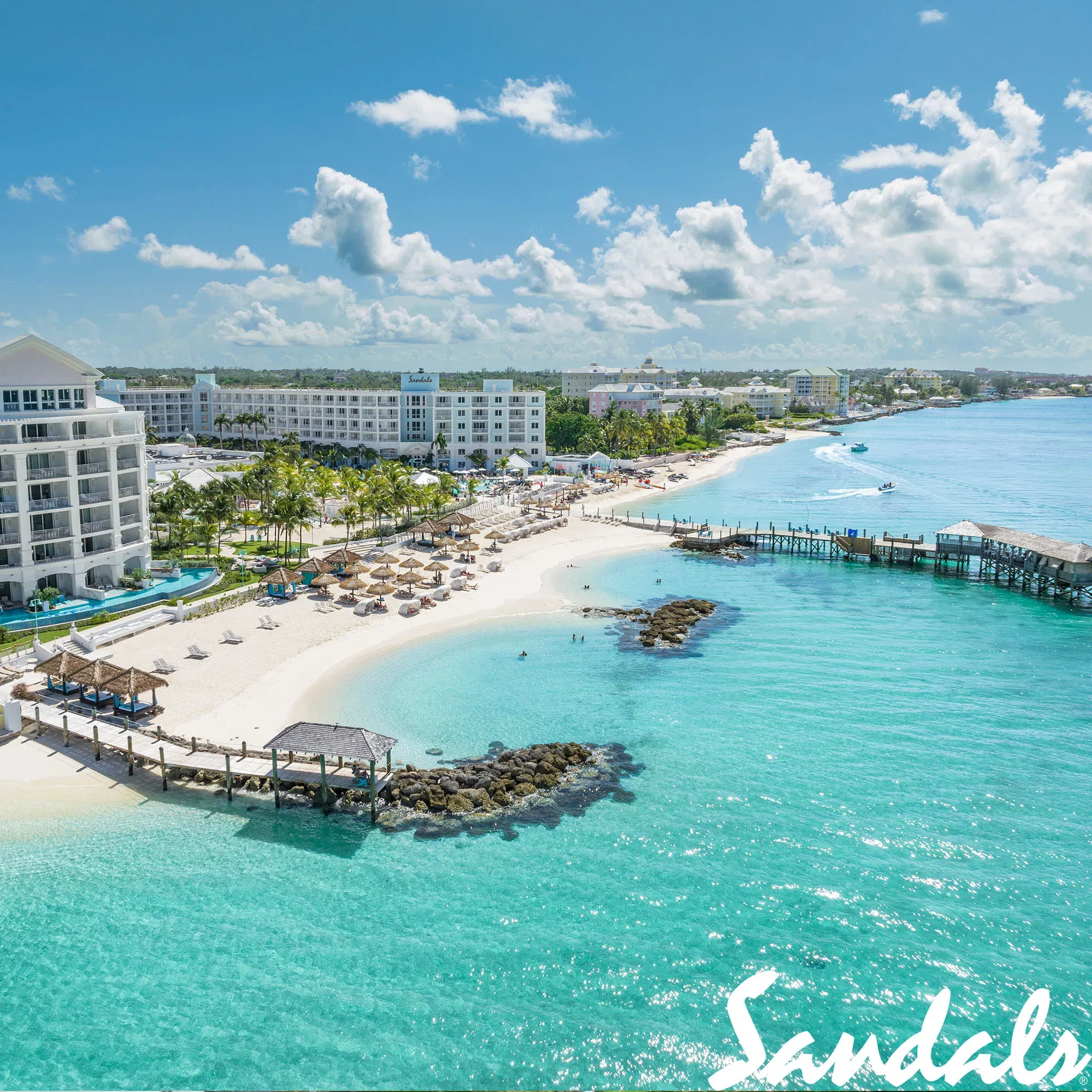 Ein weitläufiger Blick auf das Sandals Resort auf den Bahamas, mit strahlend weißen Sandstränden, tropischen Palmen und einem endlosen, türkisfarbenen Ozean. Der Strand ist perfekt für entspannte Tage am Wasser.