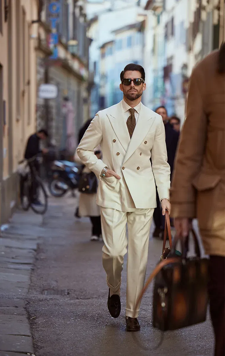 Stilvoll gekleideter Mann in cremefarbenem Anzug geht durch eine belebte Innenstadtstraße