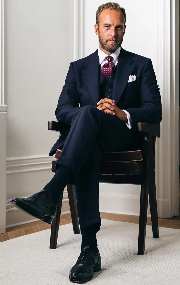 Mann in dunkelblauem Dreiteiler sitzt auf einem Stuhl und blickt direkt in die Kamera