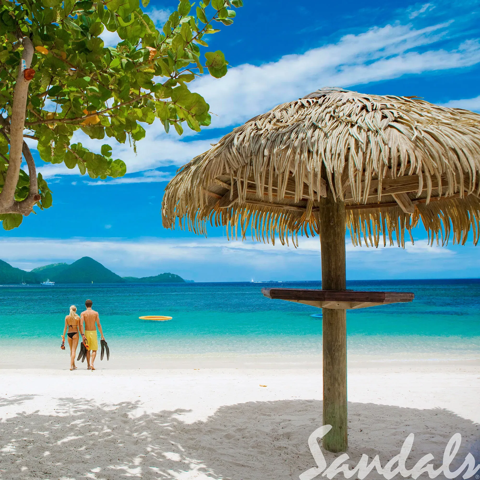 Ein Paar spaziert Hand in Hand über einen weißen Sandstrand auf St. Lucia, in Richtung des türkisfarbenen Wassers. Neben ihnen steht eine Strohhütte, und im Hintergrund sind grüne Hügel und klares, blaues Wasser zu sehen.