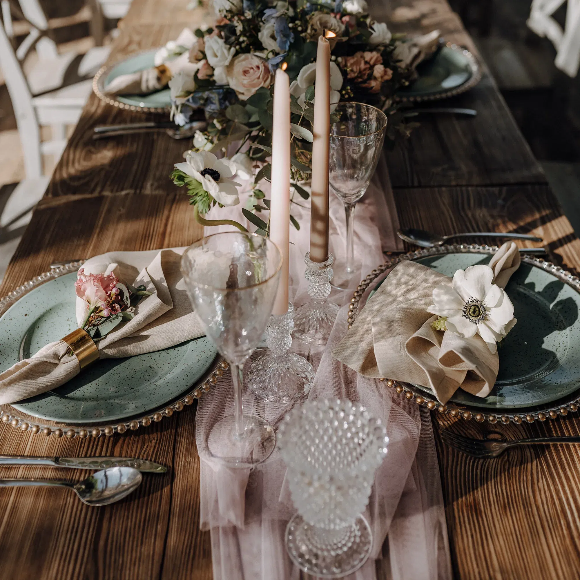 Detailaufnahme einer rustikalen Hochzeitstafel mit rosa Kerzen, Blumen und eleganten Kristallgläsern, perfekt für eine romantische Feier im Freien.