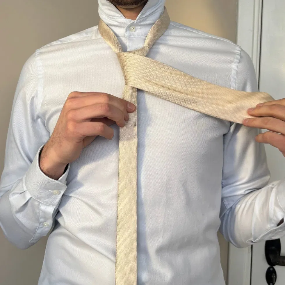 Die breite Seite der Krawatte wird über die schmale Seite nach links gelegt, um den Knoten zu formen.