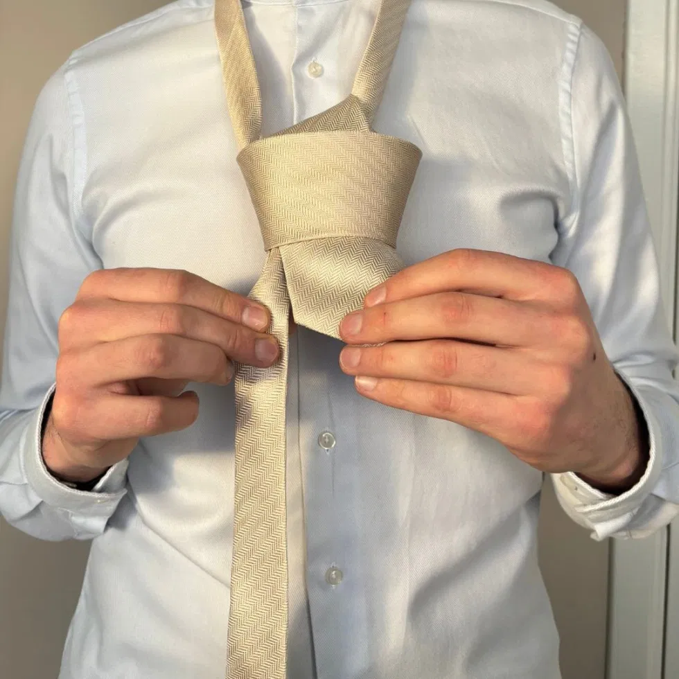 Der entstehende Krawattenknoten wird mit beiden Händen in Form gebracht.