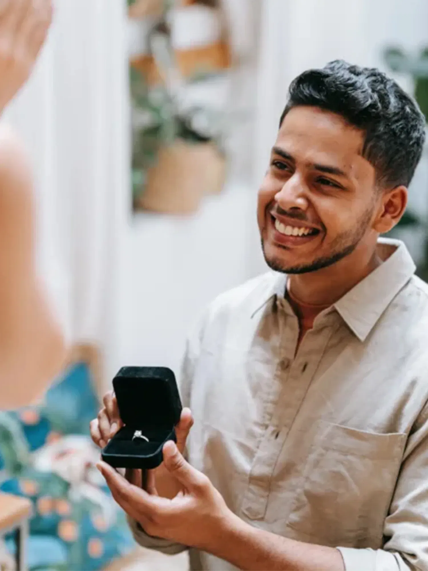 Lächelnder Mann, der einen Verlobungsring in einer schwarzen Schachtel zeigt, während er seiner Partnerin einen Antrag macht.