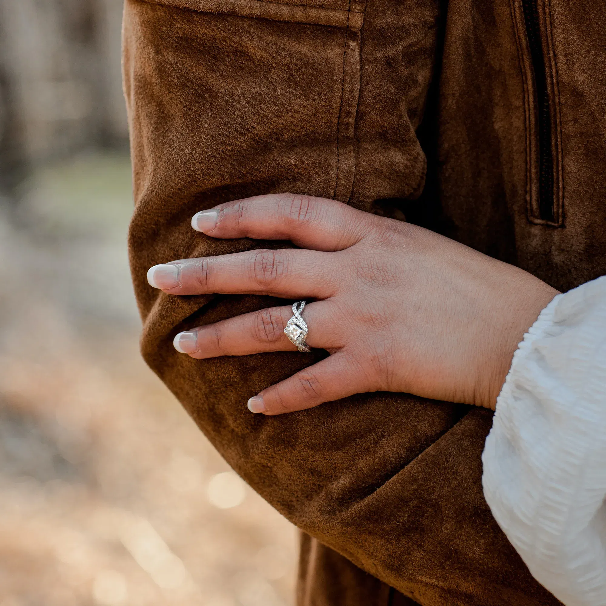 Verlobungssymbol: Hand mit elegantem Verlobungsring, die sich zärtlich an den Arm eines Partners schmiegt.