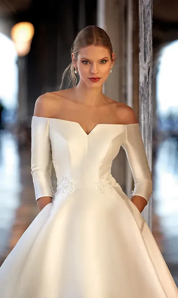 Eine Frau trägt ein stilvolles Brautkleid mit einem modernen, schulterfreien Schnitt und minimalistischen Details, perfekt für eine elegante Zeremonie.