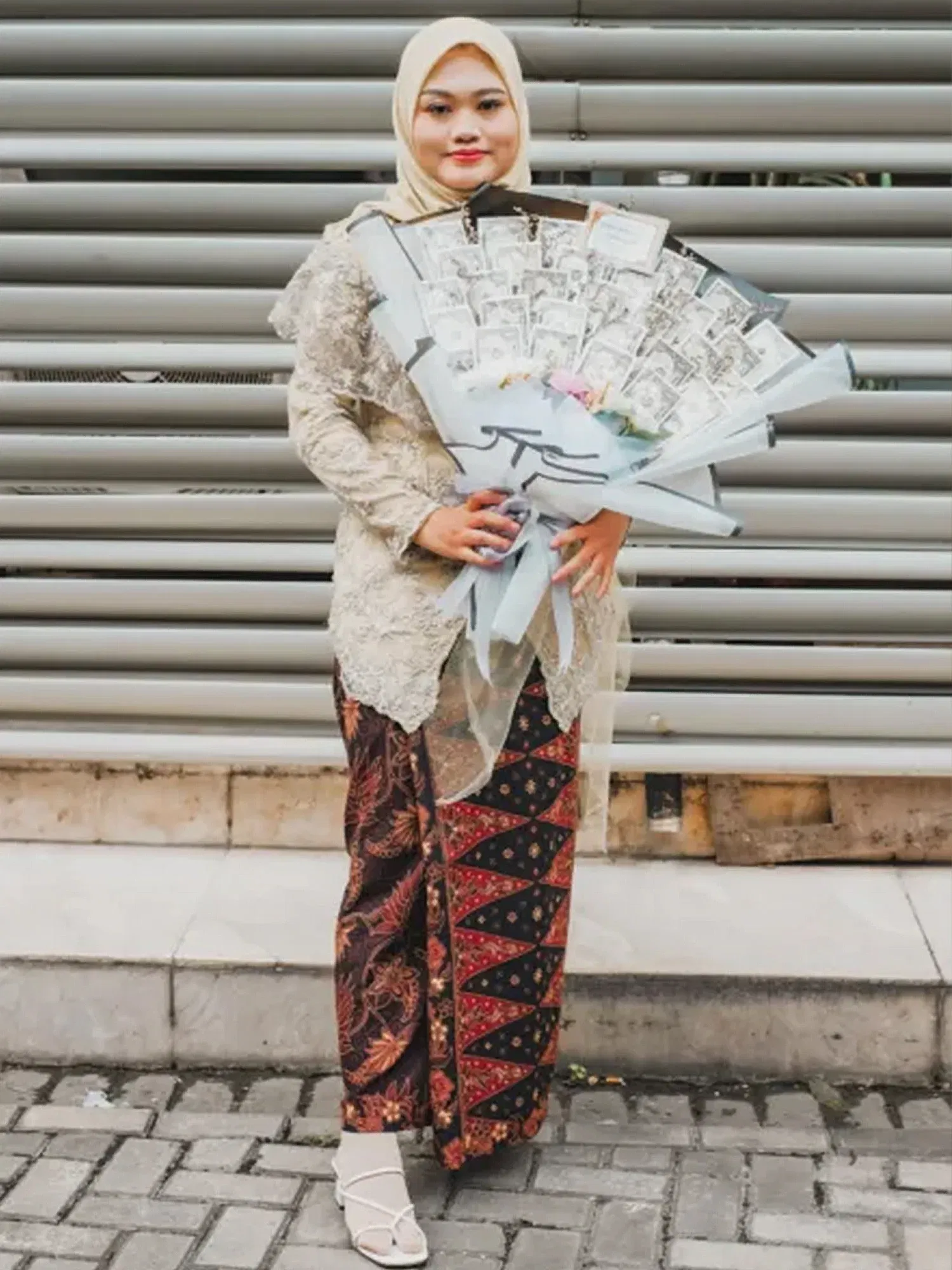 In traditioneller Tracht posiert eine Frau mit einem extravaganten Strauß aus Geldscheinen. Die Szene spielt sich vor einem industriellen Hintergrund ab.