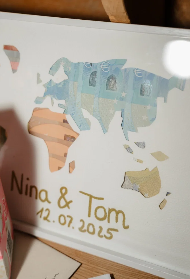 Kreatives Geldgeschenk im Bilderrahmen mit Weltkarte aus Geldscheinen sowie den Namen Nina & Tom und Hochzeitsdatum