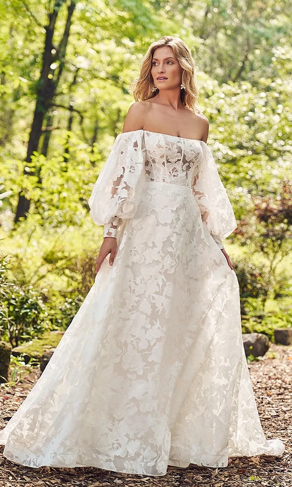 Elegante Braut in einem luftigen Spitzenkleid, umgeben von frischem Grün und natürlichem Licht.