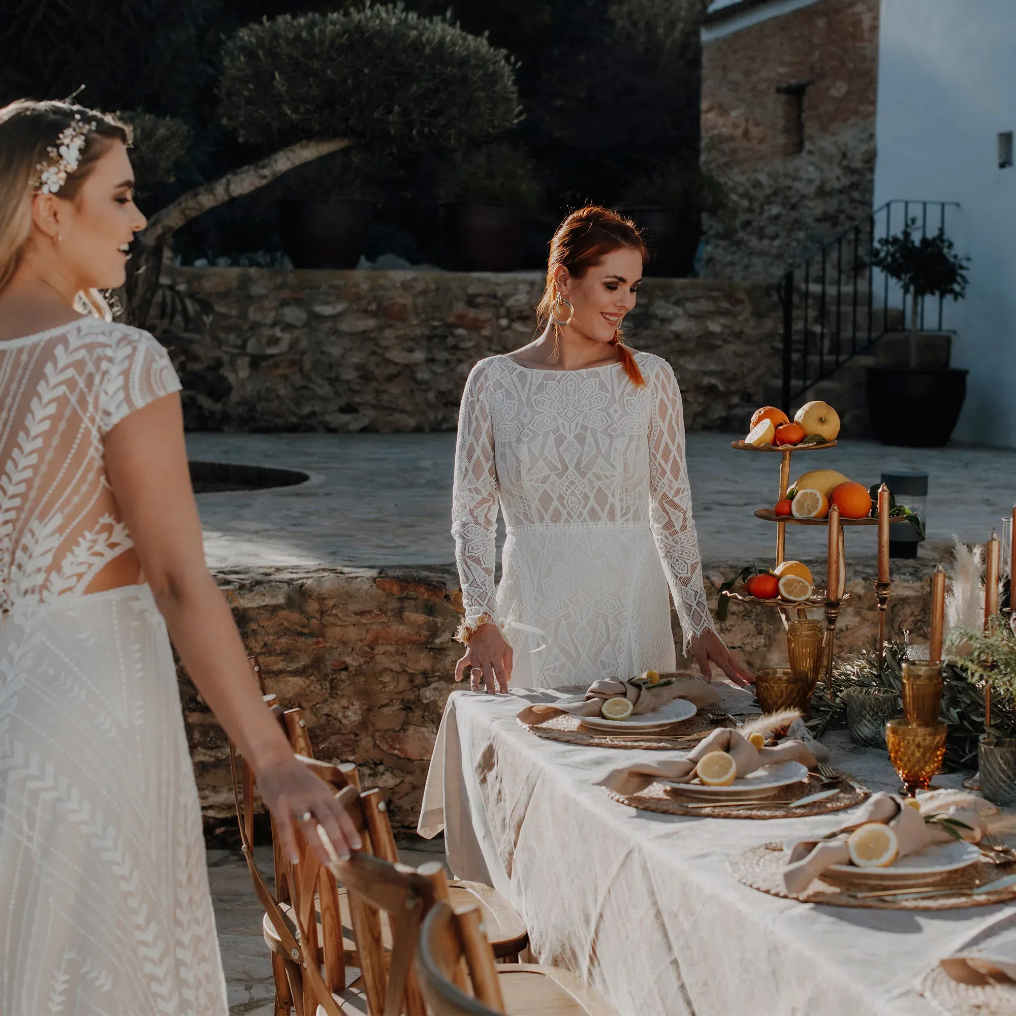 Bräute gestalten eine Hochzeitstafel mit rustikaler Tischdekoration im Freien. Auf dem Tisch liegen Zitrusfrüchte und schimmernde Kerzenhalter.