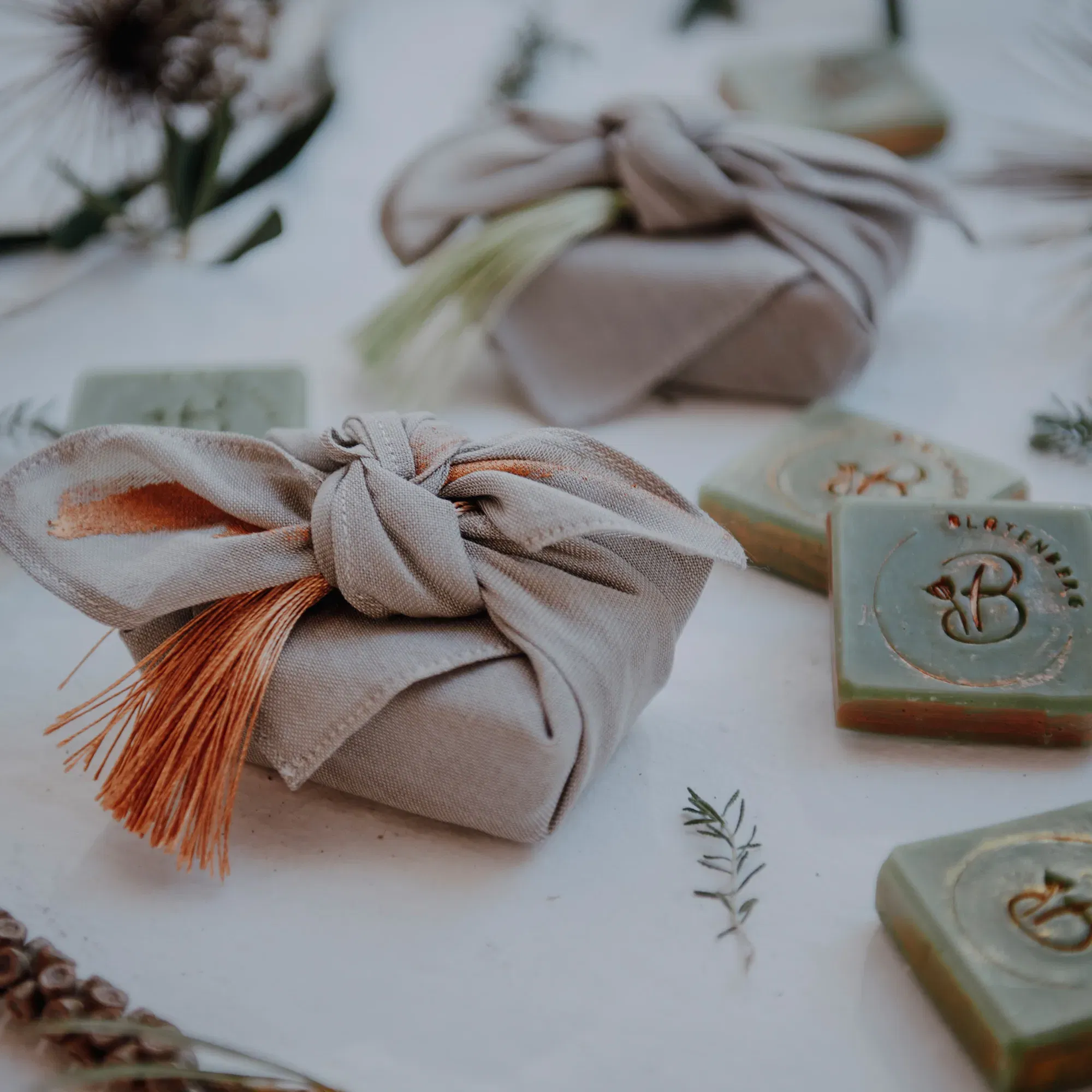 Gastgeschenke für eine Hochzeit, schön verpackt in Leinen mit natürlichen Elementen und daneben grüne Seifen als umweltfreundliche Präsente.