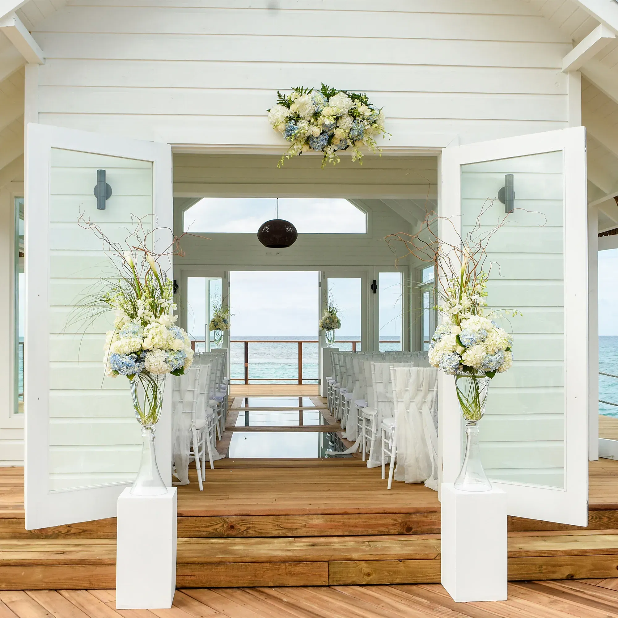 Romantische Kapelle am Meer mit schlichten weißen Stühlen und großen Blumenvasen, die zum feierlichen Anlass einladen.