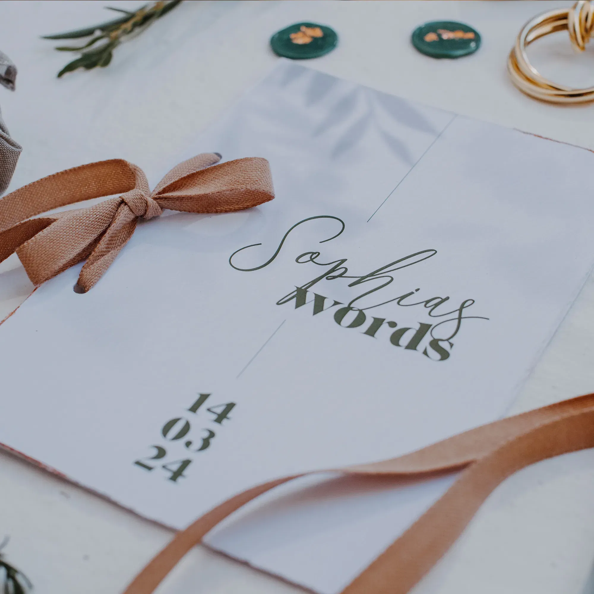 Elegante Karte mit Hochzeitsvows, verziert mit einem braunen Schleifenband, Eheringen und kleinen botanischen Verzierungen.