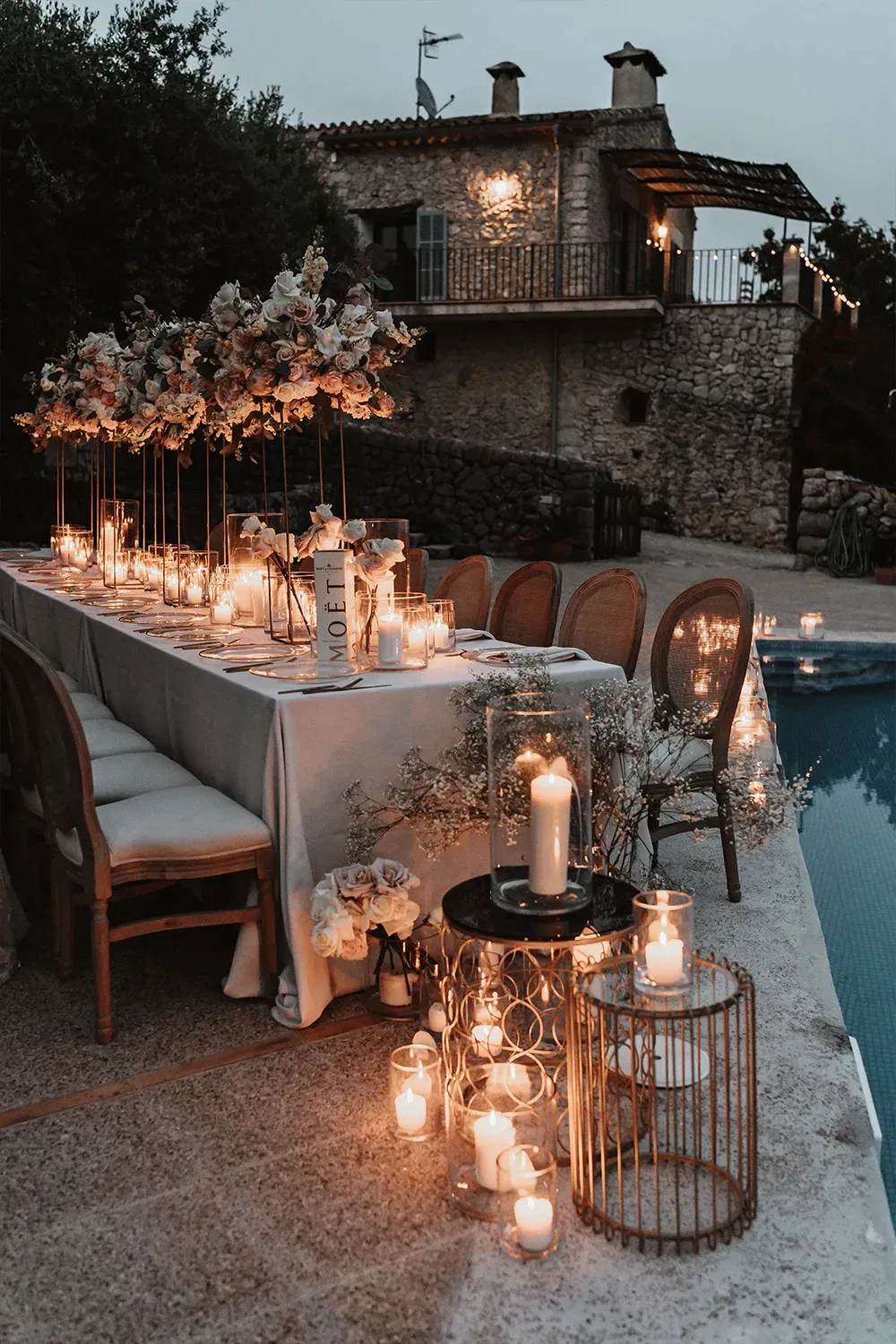 Outdoor-Hochzeitstisch mit blühenden Blumen und zahlreichen Kerzen, arrangiert in einer rustikalen, romantischen Umgebung bei Nacht.