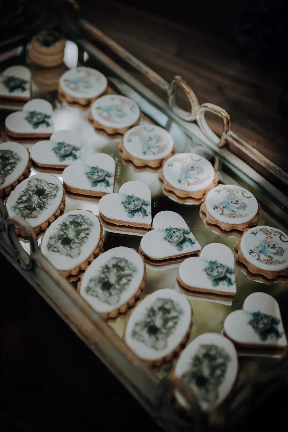 Mehrere mit Figuren und Mustern verzierte Kekse in Herz- und Ovalform, elegant auf einem Spiegeltablett für eine Hochzeitsfeier angerichtet.