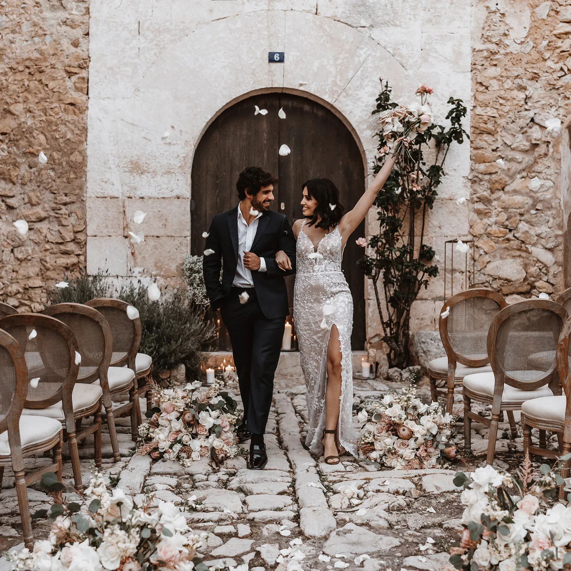 Das Brautpaar verlässt feierlich die Zeremonie, umgeben von floralen Dekorationen, während Blütenblätter in die Luft geworfen werden.