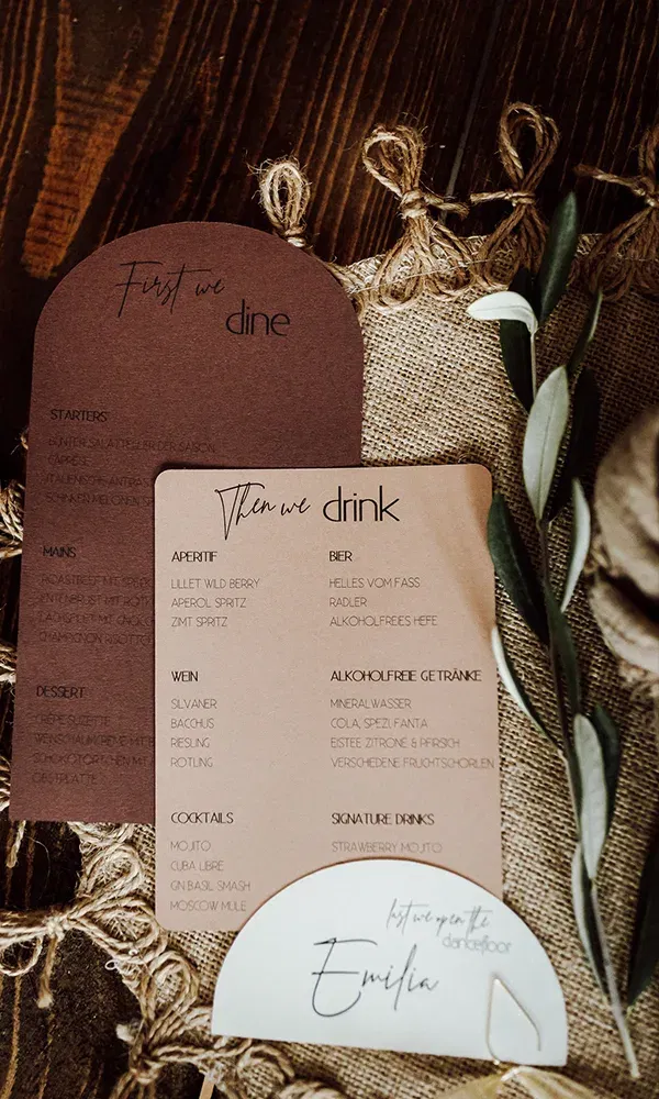 Ein Set aus Menü- und Getränkekarten in erdigen Farben, dekoriert mit Olivenzweigen und auf einem natürlichen Jutestoff arrangiert.