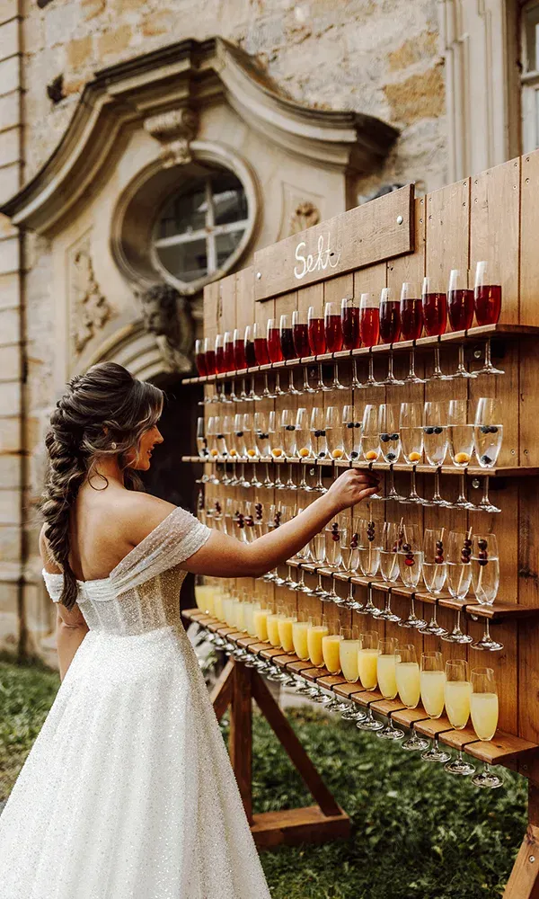 Ein festlicher Moment: Die Braut in einem funkelnden Kleid bedient sich an der Sektwand im Garten.