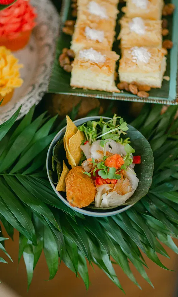 Eine dekorative Schale gefüllt mit Salat und Meeresfrüchten, serviert mit knusprigen Chips und einer frittierten Köstlichkeit, auf einer Platte mit grünen Blättern platziert.