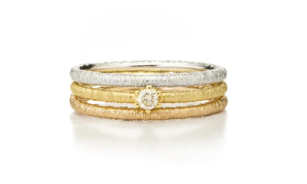 Eine elegante Kombination aus drei schmalen Ringen, die übereinander gestapelt sind. Der mittlere Ring ist mit einem glänzenden Diamanten verziert. Die matte, texturierte Oberfläche verleiht den Ringen einen einzigartigen Look.