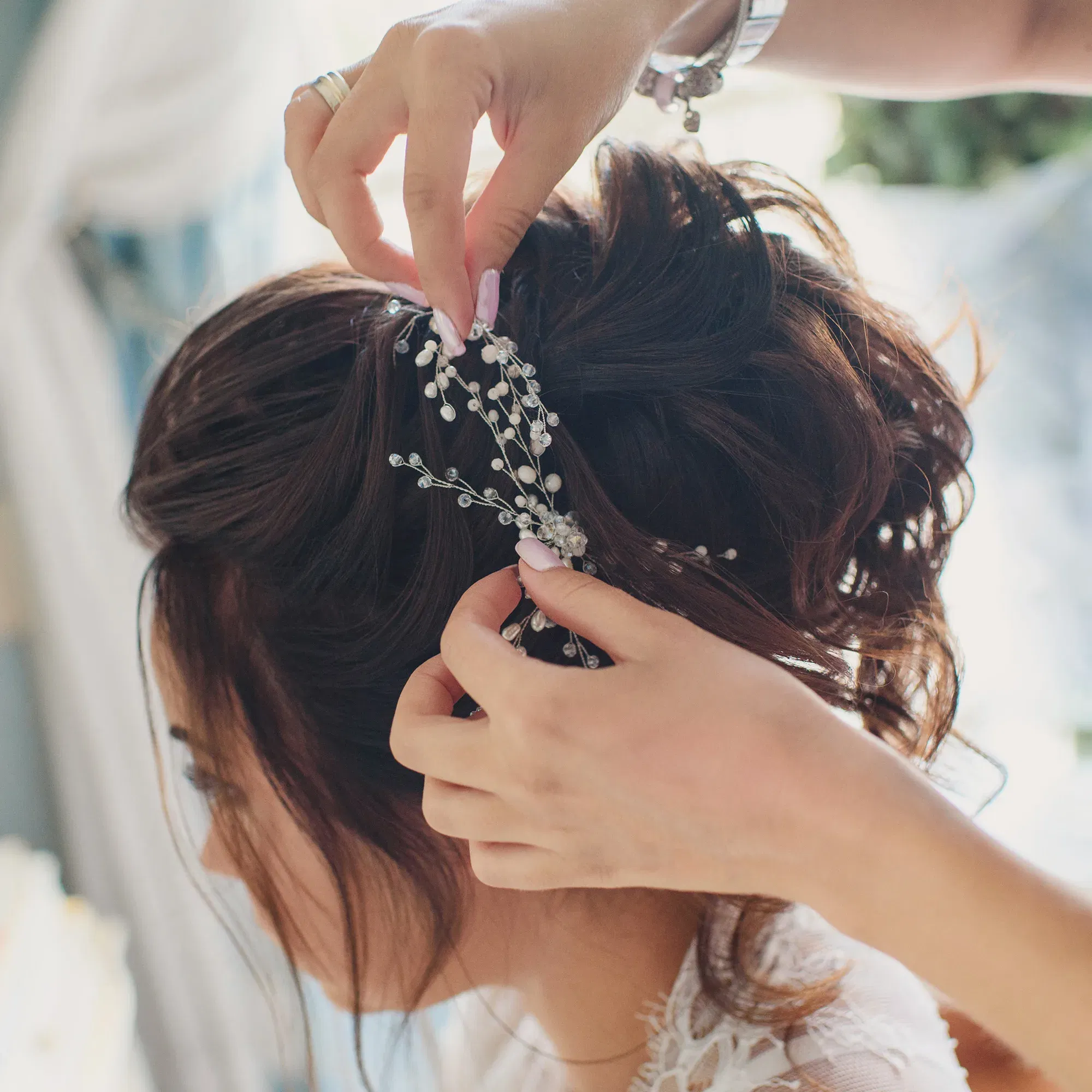Die Frisur einer Braut wird mit einer zarten, perlenbesetzten Haarnadel geschmückt. Die Szene fängt den Moment der Vorbereitung ein, während die Braut ihre Hochzeitsfrisur perfektioniert bekommt.