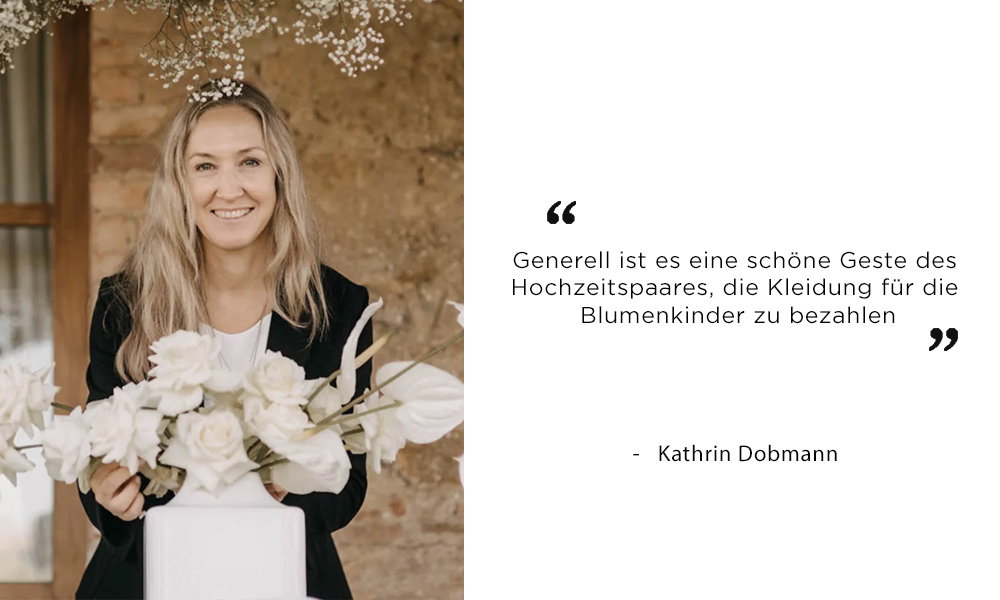 Hochzeitsplanerin Kathrin Dobmann mit langen blonden Haaren, umgeben von weißen Blumen, spricht sich in einem Zitat dafür aus, dass es eine nette Geste ist, wenn das Brautpaar die Outfits der Blumenkinder finanziert.