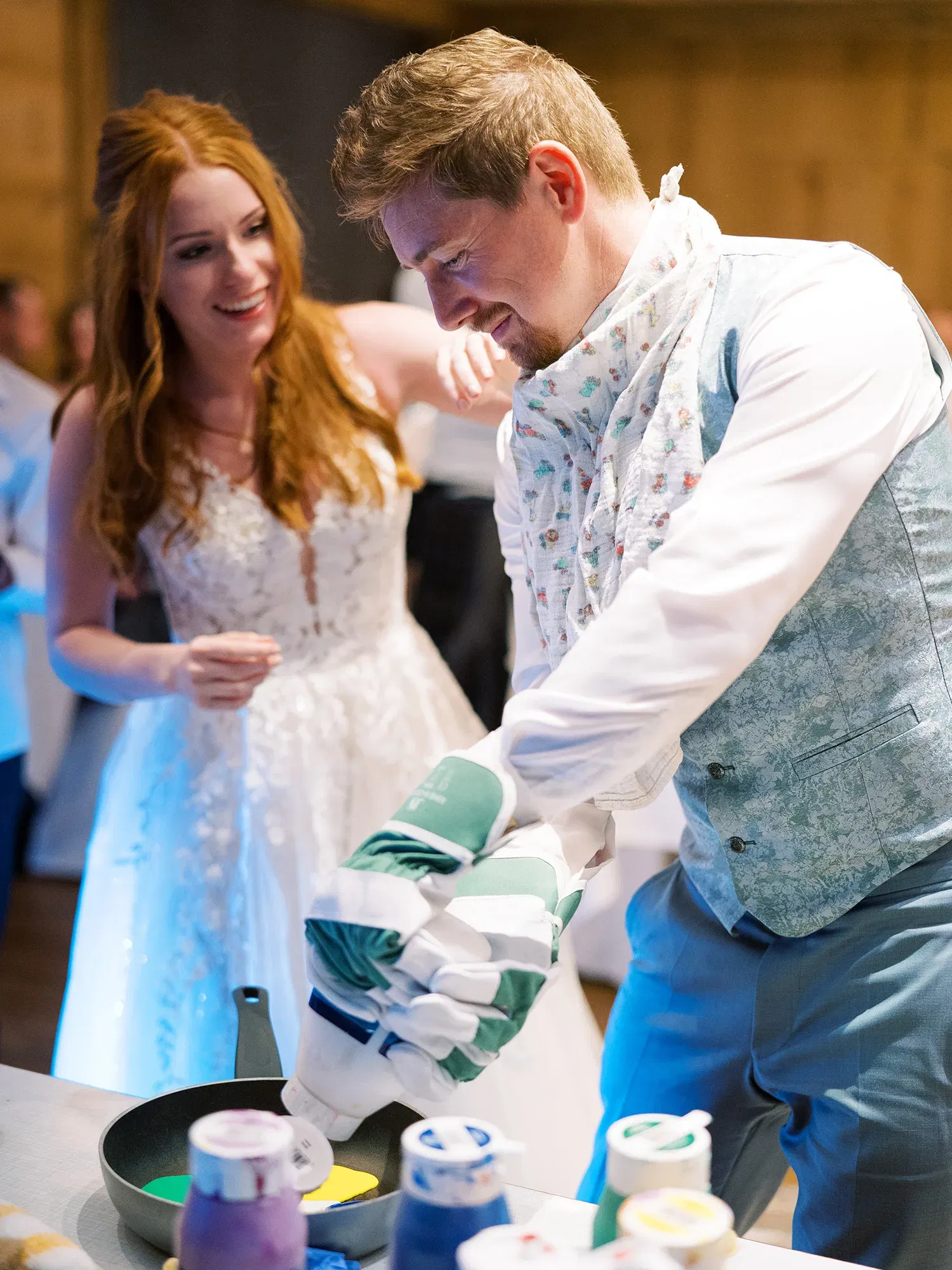 Hochzeitsspiel, bei dem der Bräutigam mit großen Gartenhandschuhen Farben mischt, die Braut steht fröhlich an seiner Seite.