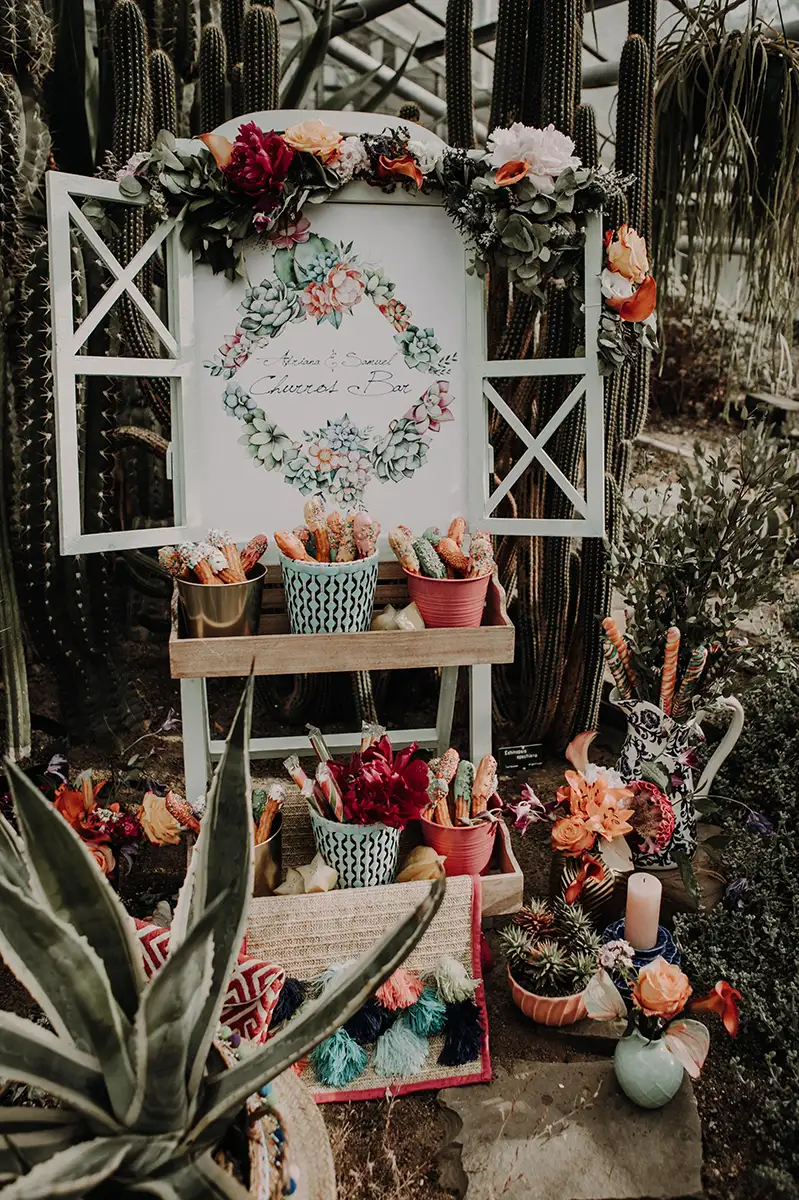 Eine liebevoll gestaltete Churros-Bar, dekoriert mit Sukkulenten und farbenfrohen Pflanzen, die eine fröhliche und lebendige Atmosphäre für die Feier schafft.