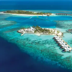 Luftaufnahme des Sangeli-Resorts mit seinen überwasser- und strandnahen Villen, umgeben von der weitläufigen, blauen Meereslandschaft.