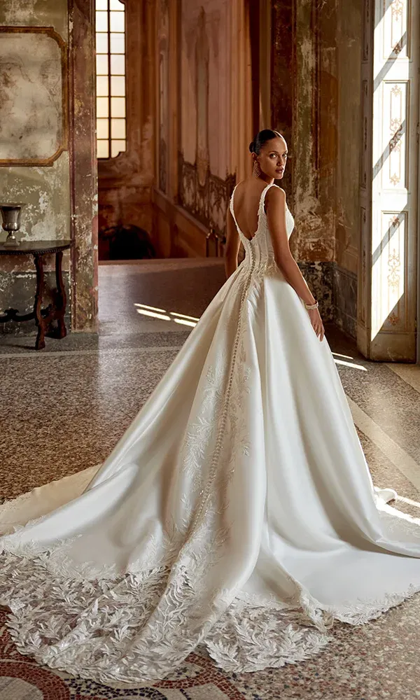 A-Linien-Brautkleid mit edler Spitze und langer Schleppe, getragen in einem historischen Palast mit verzierten Wänden und großem Fenster.