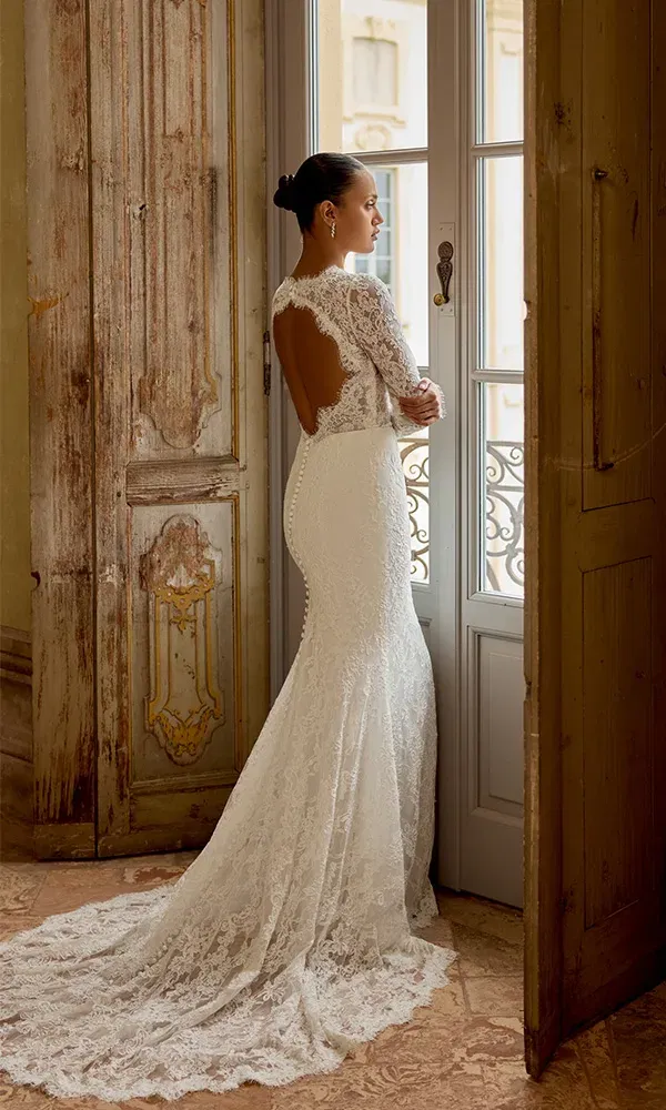 Feines Spitzenkleid mit langer Schleppe und Rückenausschnitt, stilvoll präsentiert an einem französischen Fenster mit antikem Flair.