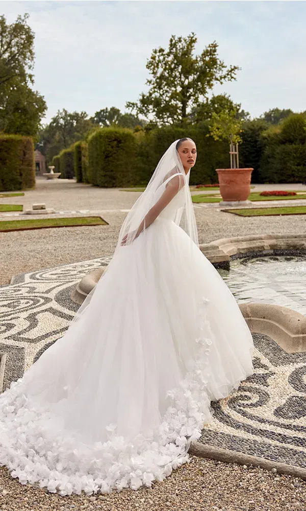 Romantisches Tüllkleid mit zarter 3D-Blütenapplikation auf der Schleppe, kombiniert mit Schleier – fotografiert im Schlosspark.