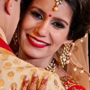 Hochzeitspaar in gold-roter Festkleidung, die Braut umarmt den Bräutigam und schaut strahlend in die Kamera.