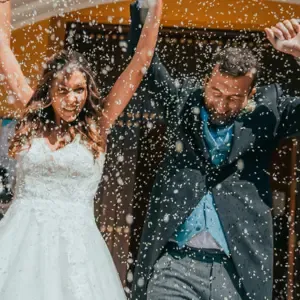 Brautpaar kommt strahlend aus dem Gebäude, hebt die Arme nach oben und Konfetti fällt auf sie herab.