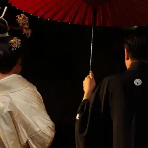 Japanisch angehauchtes Brautpaar von hinten unter einem roten Schirm.