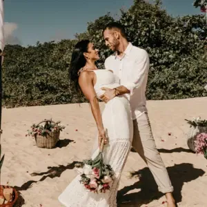 Brautpaar steht am Strand unter einem Bogen und die Braut liegt zurück gelehnt seitlich im Arm ihres Mannes.