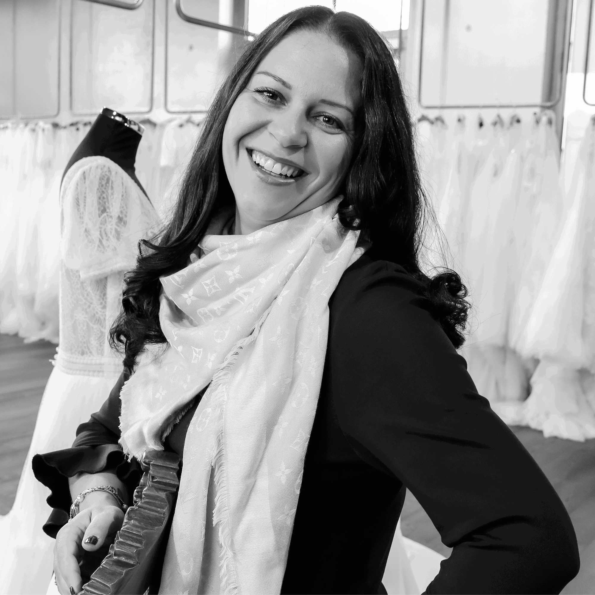 Annika Isenegger-Meister lacht in die Kamera, im Hintergrund sind verschiedene Brautkleider zu sehen.