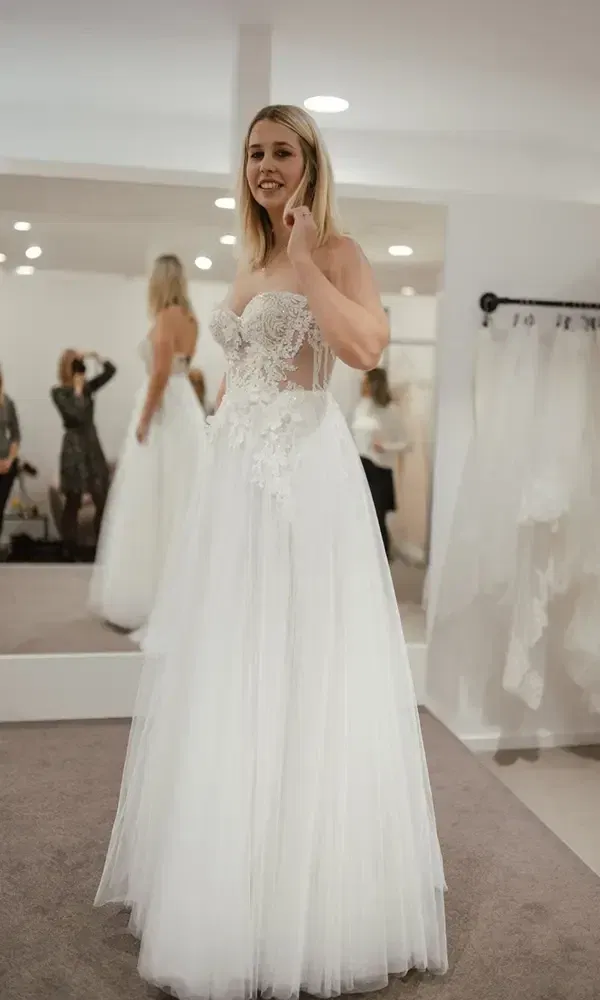 Die Braut im Ankleidezimmer probiert ein aufwendig besticktes, weißes Brautkleid für ihren großen Tag an.