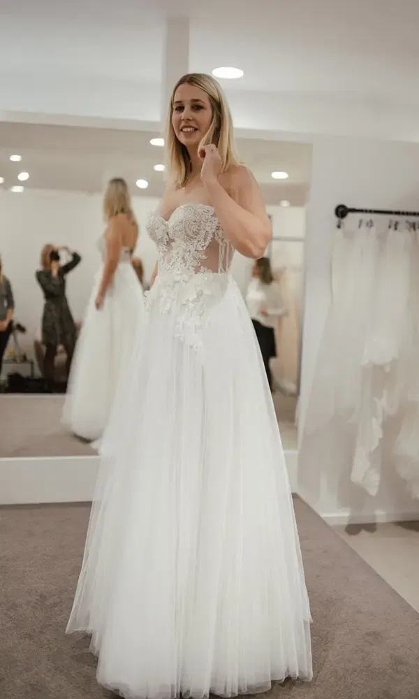 Die Braut im Ankleidezimmer probiert ein aufwendig besticktes, weißes Brautkleid für ihren großen Tag an.