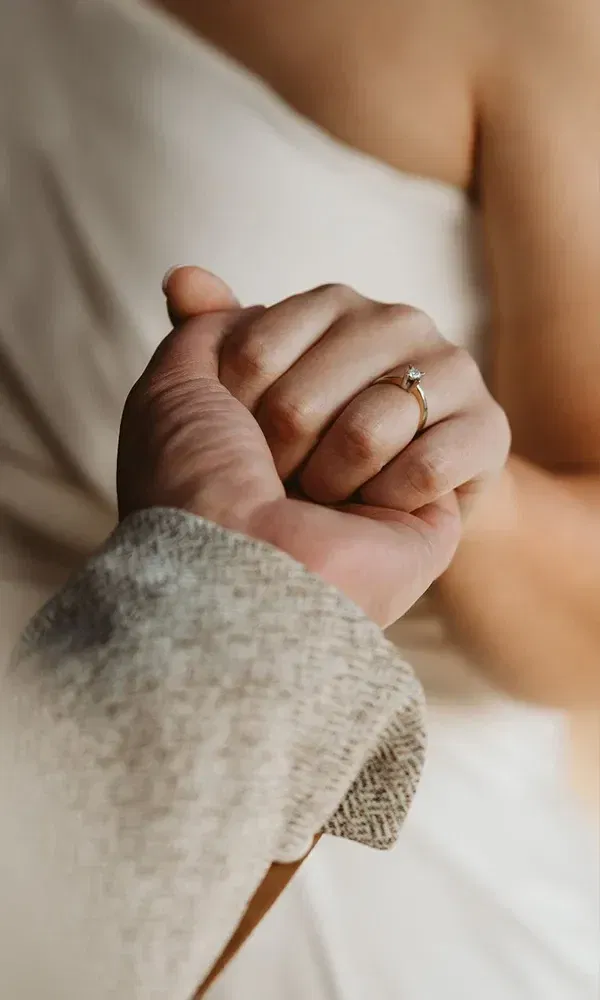 Eine Großaufnahme des Verlobungsrings an der Hand der Frau, während sie die Hand ihres Partners hält. Der Ring funkelt und hat einen Solitär-Diamanten.