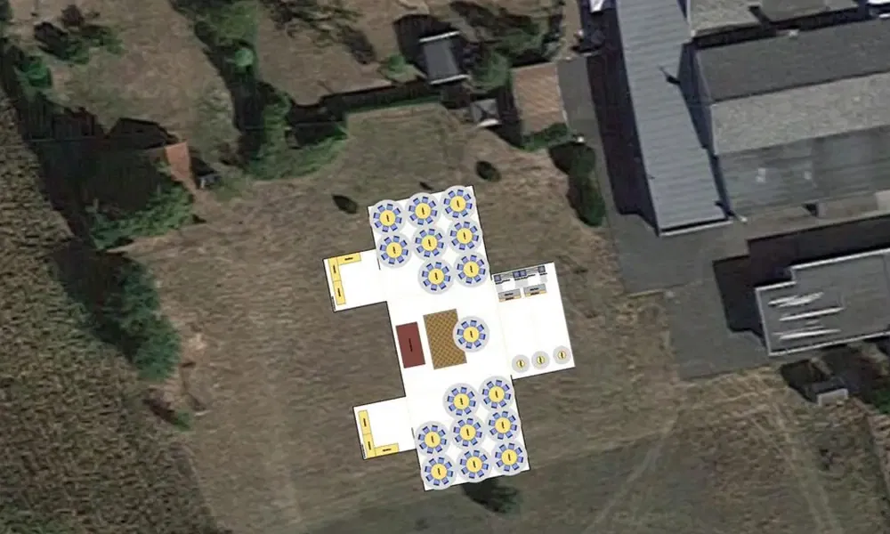 Übersichtsbild eines Hochzeitsempfangs im Freien, bei dem ein großes Zelt mit Tischen und Stühlen in einer geordneten Anordnung auf einer Wiese platziert ist. Das Zelt liegt neben einem Gebäudekomplex.