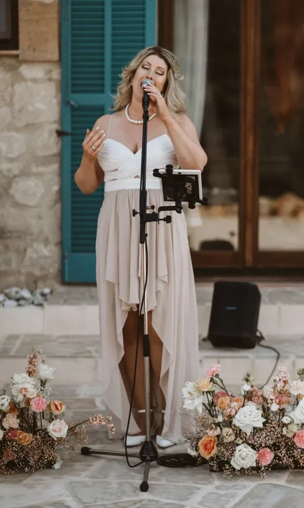 Eine Sängerin in einem eleganten Kleid trägt gefühlvoll ein Lied vor, umgeben von liebevoll arrangierten Blumenarrangements.