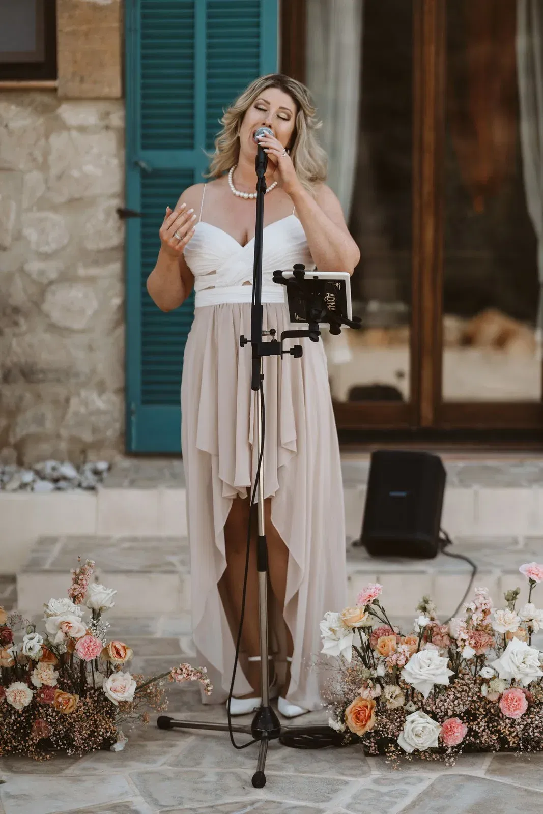 Eine Sängerin in einem eleganten Kleid trägt gefühlvoll ein Lied vor, umgeben von liebevoll arrangierten Blumenarrangements.