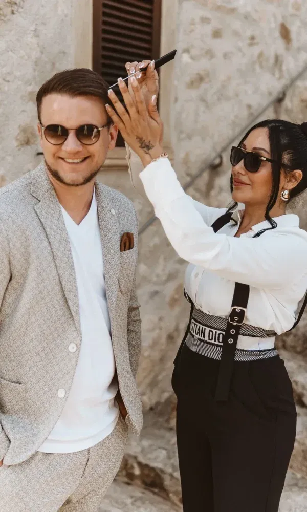 Stylistin sorgt für den perfekten Haarlook des Bräutigams, während er lächelnd in die Kamera schaut.