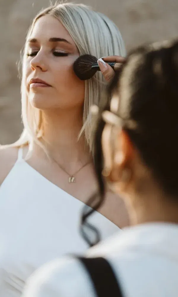 Make-up-Künstler schminkt die Braut sorgfältig, während sie die Augen geschlossen hält und entspannt wirkt.