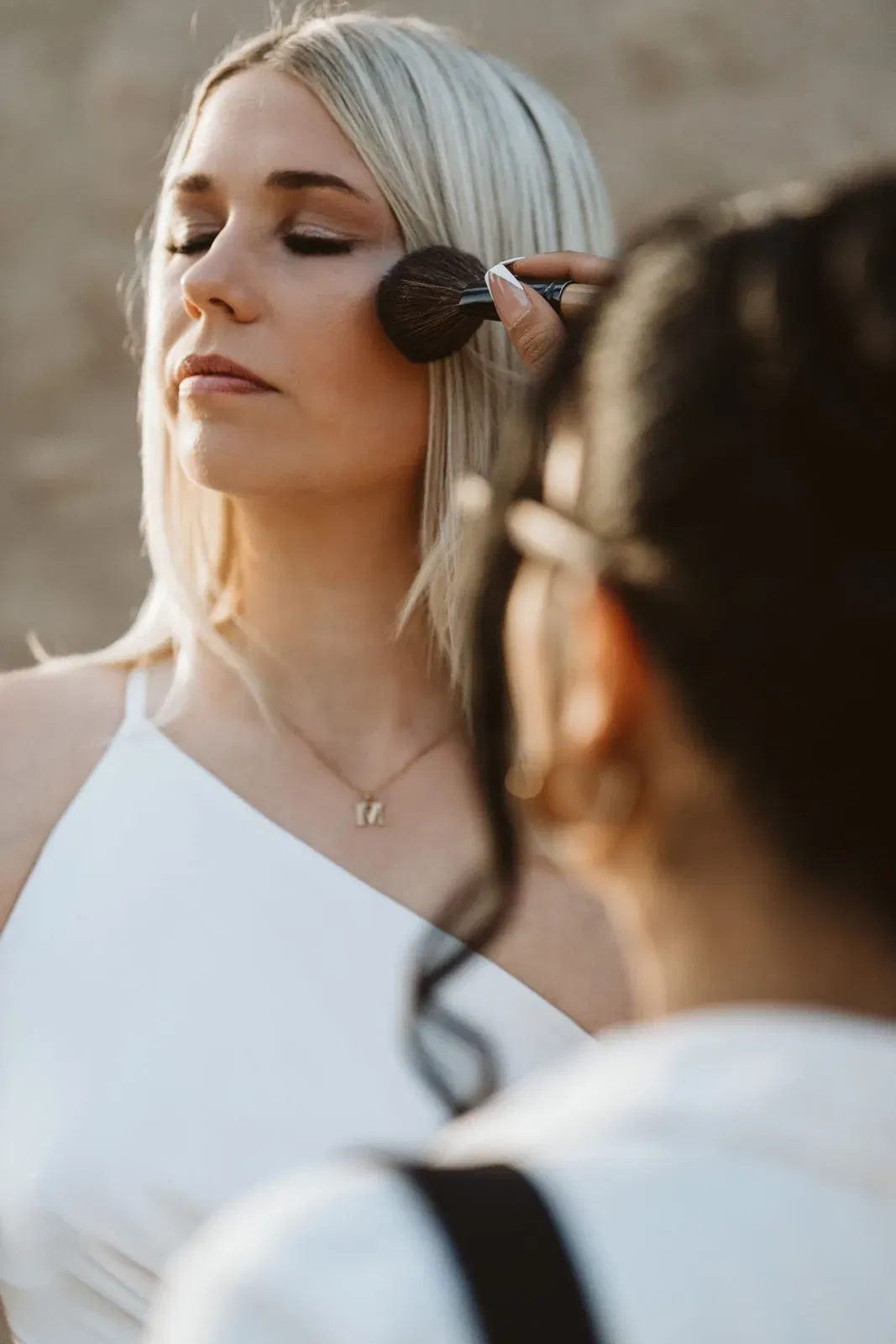 Make-up-Künstler schminkt die Braut sorgfältig, während sie die Augen geschlossen hält und entspannt wirkt.